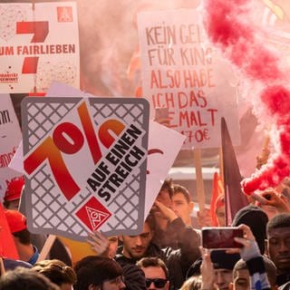 In Bayern nehmen Menschen mit Plakaten und Fahnen an einer Auftaktdemonstration der Tarifverhandlungen für die Metall- und Elektroindustrie teil. Die IG Metall fordert sieben Prozent mehr Lohn für Beschäftigte - die ersten Tarifverhandlungen starten heute in Baden-Württemberg, Bayern und Sachsen.