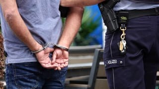 Ein Mann steht in Handschellen neben einem Polizisten. Die Zahl der politisch motivierten Straftaten in BW ist im ersten Halbjahr 2024 gestiegen.