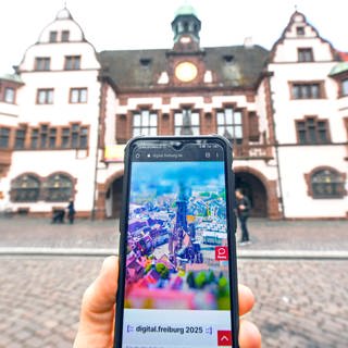 Auf einem Smartphone vor dem Freiburger Rathaus ist die Webseite "Digital.freiburg.de" geöffnet.