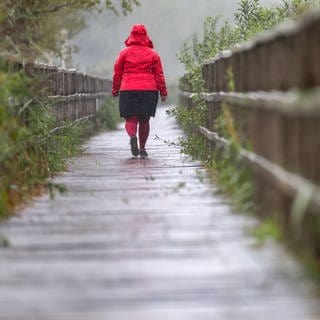 Eine Frau mit Regenjacke läuft im Regen den Federseesteg entlang.