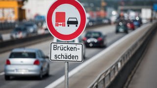 Ein Hinweisschild "Brückenschäden" steht auf einer Brücke, die von Autos befahren wird.