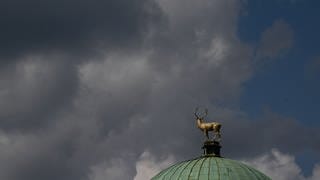 Ein Mix aus dunklen Wolken und blauem Himmel erscheint über der Figur des goldenen Hirschen auf dem Kunstgebäude. Das Wetter in Baden-Württemberg war im September besonders nass und kalt.