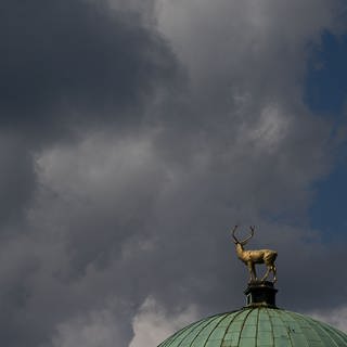 Ein Mix aus dunklen Wolken und blauem Himmel erscheint über der Figur des goldenen Hirschen auf dem Kunstgebäude. Das Wetter in Baden-Württemberg war im September besonders nass und kalt.