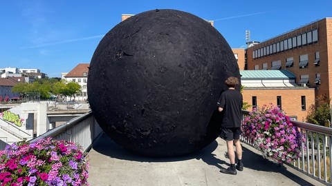 Ein großer, schwarzer Filsball wird über eine schmale Brücke gerollt - die Aktion ist Teil eines Kunstprojekts im Rahmen der Ornamenta