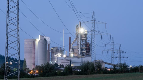 Strommasten stehen im Morgenlicht vor einem Zementwerk im Kreis Rottweil. 