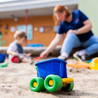 Ein Kind spielt mit einer Erzieherin im Sandkasten einer Kita.