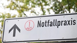 Auf einem Wegweiser an einer Straße vor einem Krankenhaus steht ein Hinweisschild auf eine Notfallpraxis. In einem gemeinsamen Brief kritisieren 18 Bürgermeisterinnen und Bürgermeister die Pläne der KVBW zur Schließung der Notfallpraxen und fordern Gesundheisminister Manfred Luche (Grüne) dazu auf, zu intervenieren.