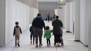 Eine Flüchtlingsfamilie geht durch die zu einer Massenunterkunft umfunktionierten Messehalle. Baden-Württemberg fordert von der Bundesregierung härtere Regeln bei der Asyl- und Migrationspolitik.