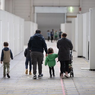 Eine Flüchtlingsfamilie geht durch die zu einer Massenunterkunft umfunktionierten Messehalle. Baden-Württemberg fordert von der Bundesregierung härtere Regeln bei der Asyl- und Migrationspolitik.