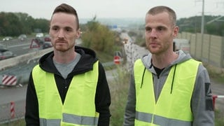 Zwei Männer in Warnweste stehen an der Autobahn