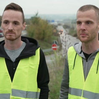 Zwei Männer in Warnweste stehen an der Autobahn