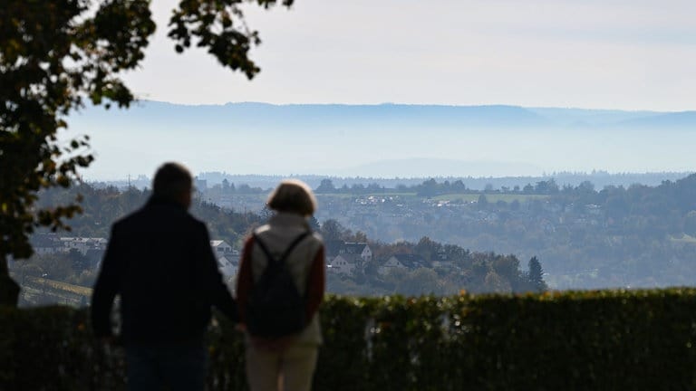 Spaziergänger spazieren am Württemberg vor der Kulisse der im Herbstnebel erscheinenden Schwäbischen Alb.