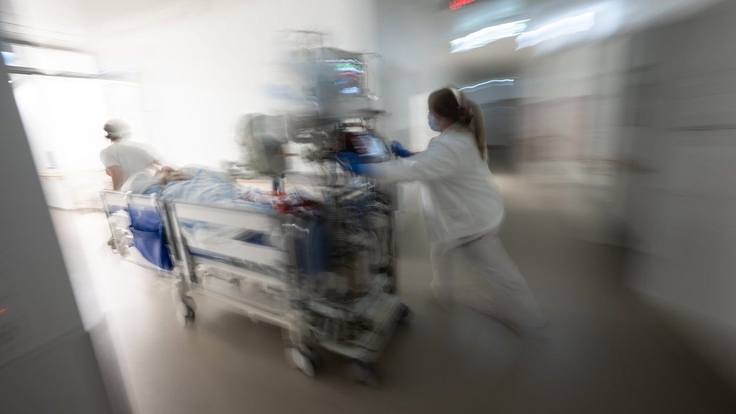 Eine Pflegerin fährt eine Intensivpatientin in einem Krankenbett durch einen Gang einer Klinik.