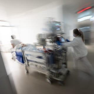 Eine Pflegerin fährt eine Intensivpatientin in einem Krankenbett durch einen Gang einer Klinik.