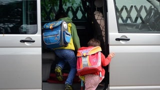 Zwei Kinder steigen in ein Auto.