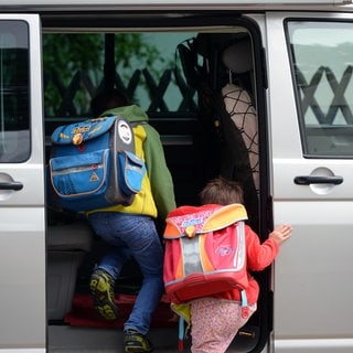 Zwei Kinder steigen in ein Auto.