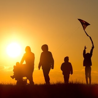 Eine Familie mit Kinderwagen und einem Drachen an der Schnur geht bei Sonnenuntergang über einen Weg durch die Salzwiesen im Watt bei Westerhever (Symbolbild).