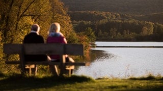 Zwei Personen sitzen in Zaberfeld (Kreis Heilbronn) vor dem See Ehmentsklinge auf einer Bank. 