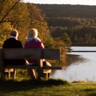 Zwei Personen sitzen in Zaberfeld (Kreis Heilbronn) vor dem See Ehmentsklinge auf einer Bank. 