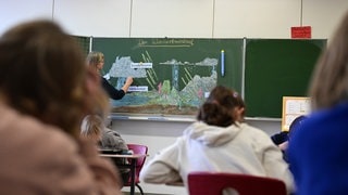 Eine Lehrerin erklärt der Klasse den Wasserkreislauf. Damit künftig weniger Unterricht ausfällt, fordern  Bildungsverbände mindestens 1.500 zusätzliche Lehrerstellen.