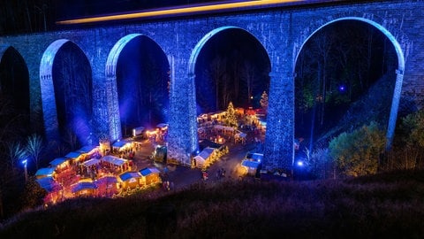 Die Höllentalbahn fährt über das beleuchtete Viadukt über der Ravennaschlucht, während darunter der Weihnachtsmarkt stattfindet.