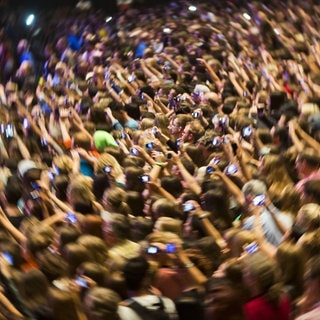 Symbolbild: Auf dem Foto stehen Konzertbesucher dicht an dicht. Fast alle halten ihre Smartphones nach oben um die Bühne zu filmen.