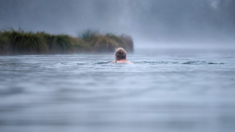 Eine Frau schwimmt bei einstelligen Temperaturen und Nebel im Schwarzachtalsee.