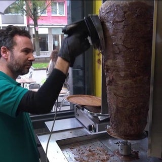 EIn Mann schneidet Fleisch von einem Dönerspieß