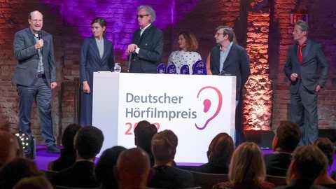 Die Preisträger in der Kategorie "Dokumentation" stehen bei der Verleihung des 20. Deutschen Hörfilmpreises 2022 auf der Bühne (von links nach rechts: Philip Klenk, Christiane Nothofer, Erico Zeyen, Silke Bauer, Clemens Trötzmöller und der Laudator Roman Knižka). 