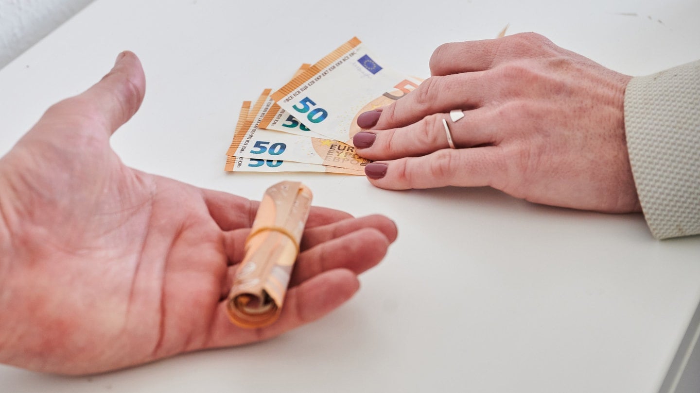 Eine Männerhand (l) hält ein Bündel 50-Euro-Scheine, während eine Frauenhand weniger 50-Euro-Scheine hält.