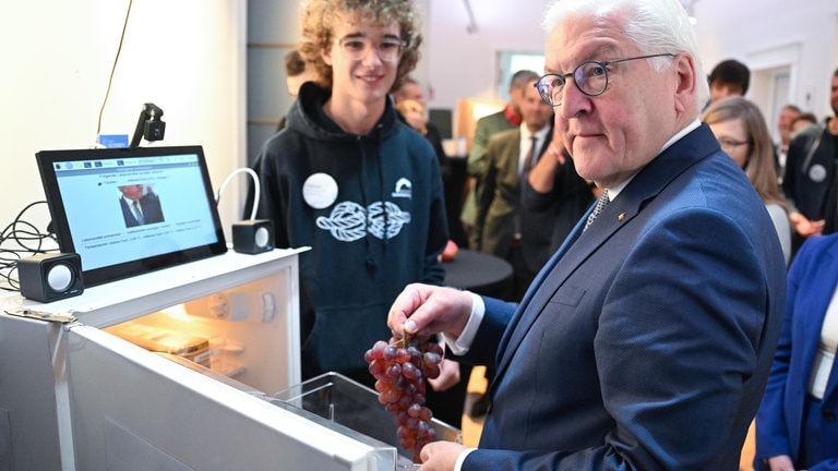 Bundespräsident Frank-Walter Steinmeier (r) sieht sich beim Finale des Bundeswettbewerbs Künstliche Intelligenz ein Projekt des intelligenten Kühlschranks von Fabian Then (l) an und hält dabei Weintrauben in der Hand.