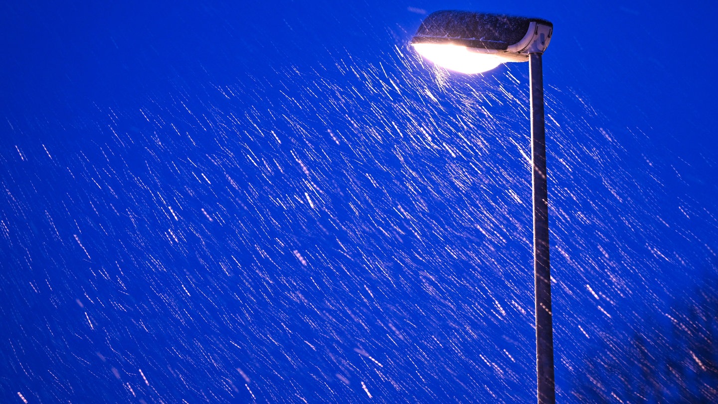 Leichter Schneefall am Abend. Eine Straßenlaterne leuchtet.