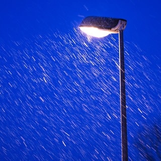 Leichter Schneefall am Abend. Eine Straßenlaterne leuchtet.