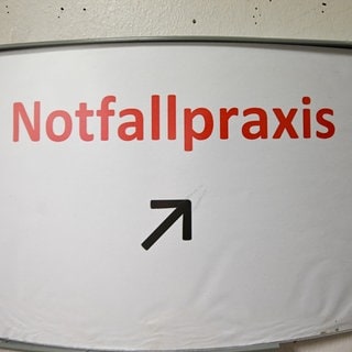 Ein Schild mit der Aufschrift Notfallpraxis ist an einer Wand angebracht.