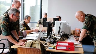 Archivbild: Mehrere Menschen in Bundeswehr-Uniform arbeiten bei einer Stabsrahmenübung der Bundeswehr an einem Schreibtisch.