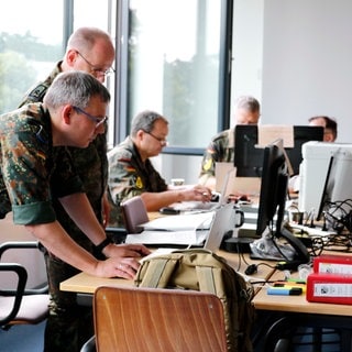 Archivbild: Mehrere Menschen in Bundeswehr-Uniform arbeiten bei einer Stabsrahmenübung der Bundeswehr an einem Schreibtisch.