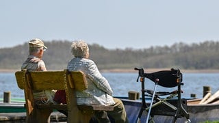 Ein älteres Paar sitzt auf einer Bank an einem See. Die Lebenserwartung in BW steigt.