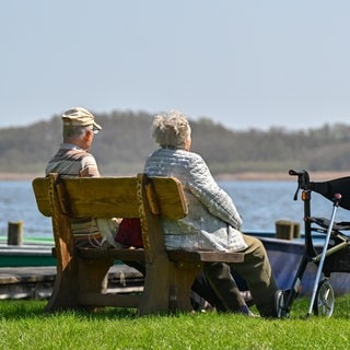 Ein älteres Paar sitzt auf einer Bank an einem See. Die Lebenserwartung in BW steigt.