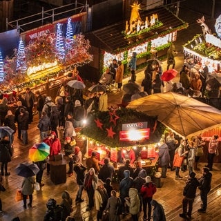 Besucher und Besucherinnen schlendern über den Stuttgarter Weihnachtsmarkt mit seinen beleuchteten Buden.