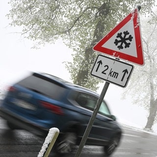 Ein Auto fährt an einem Schild vorbei, das vor Schnee auf der Schwäbischen Alb warnt. (Symbolbild)