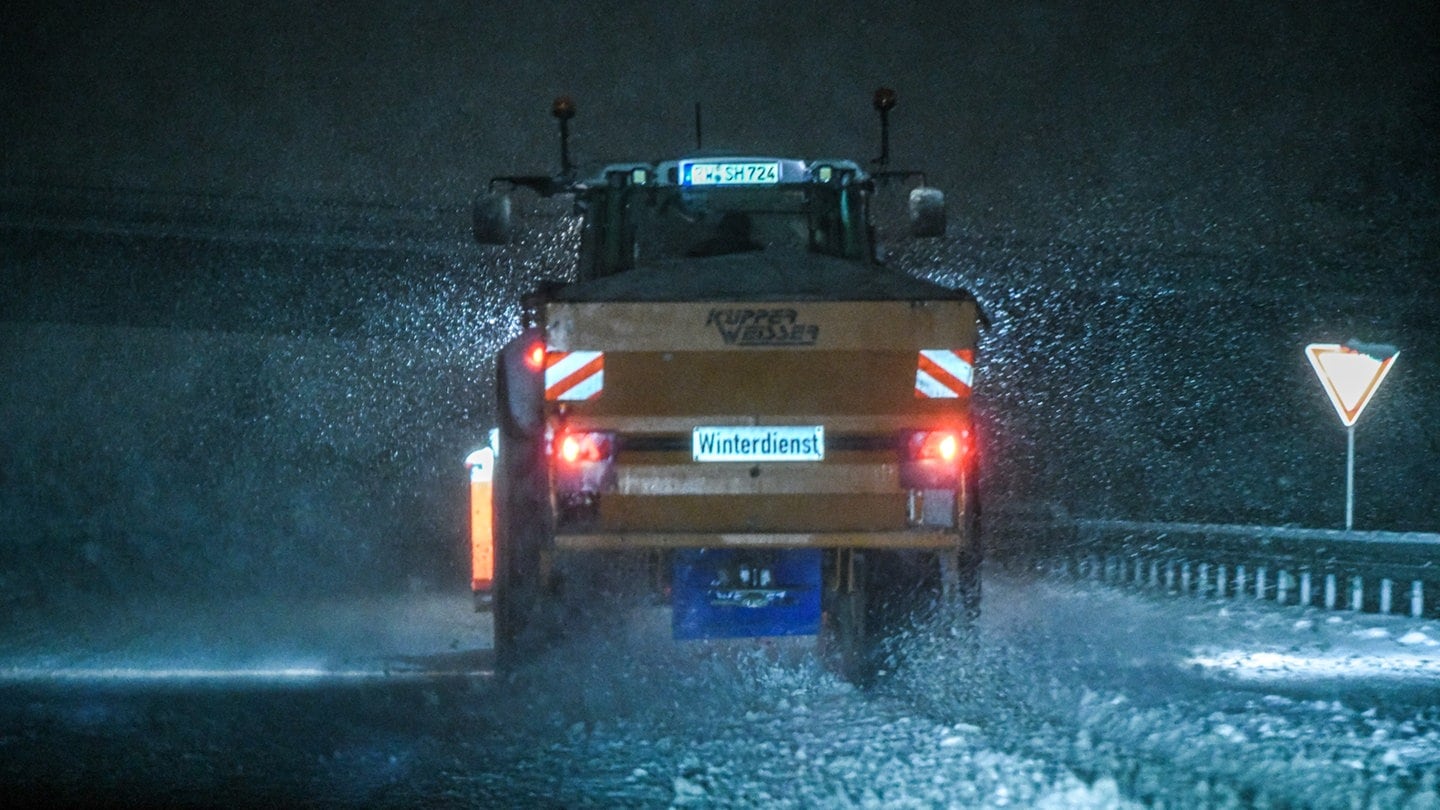 Ein Streufahrzeug fährt über eine schneebedecke Straße.