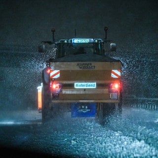 Ein Streufahrzeug fährt über eine schneebedecke Straße.