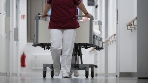 Symbolbild: Eine Krankenpflegerin und ein Krankenpfleger schieben ein Krankenbett durch den Gang einer Station eines Krankenhauses.