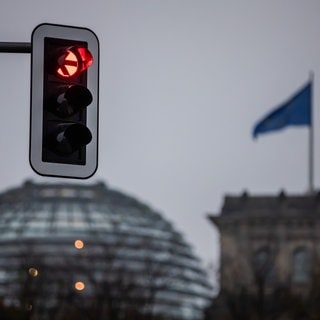 Eine Ampel leuchtet rot vor der Kuppel des Reichstagsgebäudes in Berlin. 