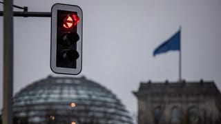 Eine Ampel leuchtet rot vor der Kuppel des Reichstagsgebäudes in Berlin. 