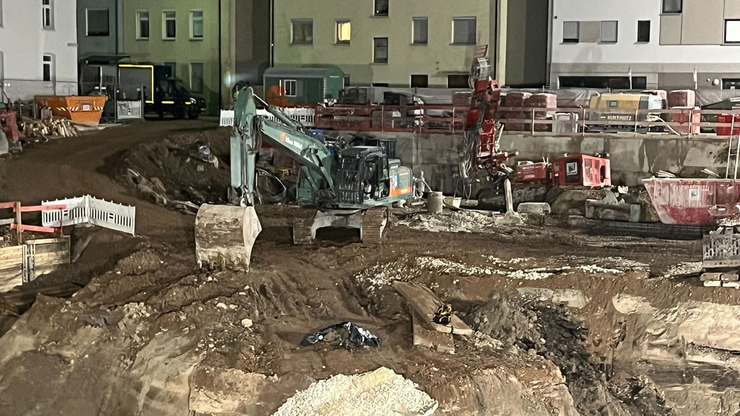 Ein Bagger steht auf einer Baustelle hinter einer Bombe, die mit einer schwarzen Plastikplane abgedeckt ist. Wegen eines Bombenfunds müssen einige Menschen in Teilen der Ulmer Innenstadt ihre Wohnungen verlassen. Bauarbeiter hätten am Nachmittag eine rund 250 Kilogramm schwere Fliegerbombe auf einer Baustelle gefunden, teilte die Polizei mit.