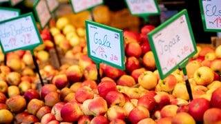 Zahlreiche Äpfel verschiedener Sorten stehen an einem Obst- und Gemüsestand auf dem Wochenmarkt in Holzkisten zum Verkauf. Preisermittlerin Nadine Maldacker prüft jeden Monat Preise und trägt dazu bei, die Inflation zu ermitteln.