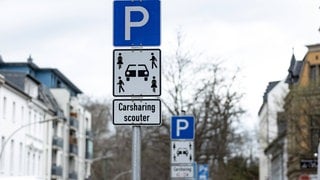 Ein Verkehrsschild mit der Aufschrift "Carsharing" steht an einer Straßen und markiert einen Parkplatz. 