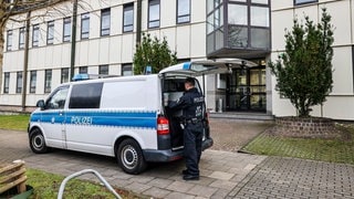 Ein Polizeibeamter der Bundespolizei steht an einem Polizeiauto vor einer Flüchtlingsunterkunft in Essen. In Nordrhein-Westfalen und Baden-Württemberg ist es am Morgen zu einem Polizeieinsatz im Zusammenhang mit einer internationalen Razzia gegen ein Schleuser-Netzwerk gekommen.