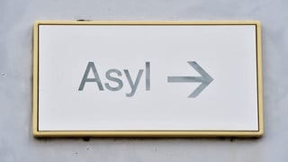 Ein Schild mit der Aufschrift "Asyl" hängt bei einer Landeserstaufnahme für Asylbewerber (LEA) an der Wand.